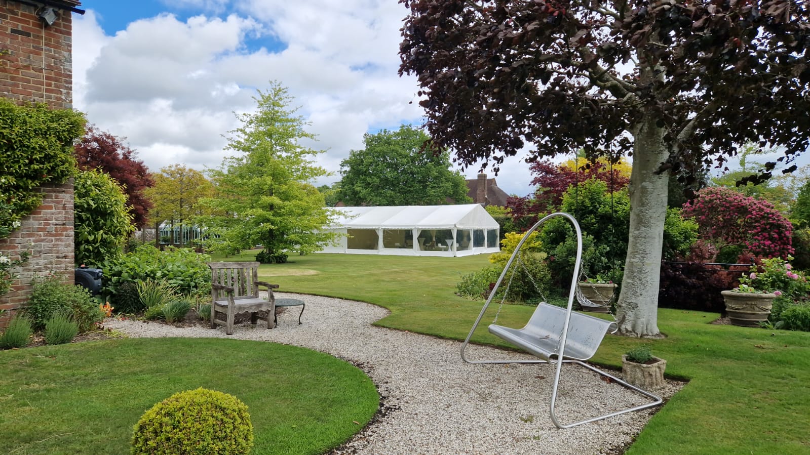 Distant white marquee set within a formal garden, with gravel paths, seating and mature planting